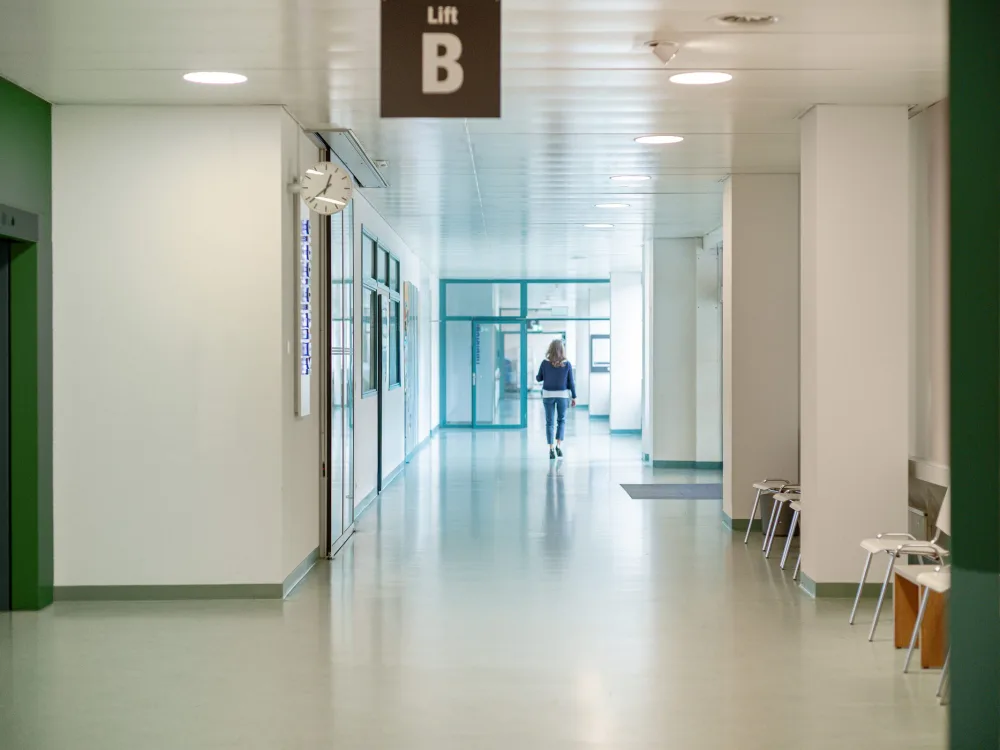 Heller Korridor eines Spitals, eine Person geht dem Tageslicht entgegen