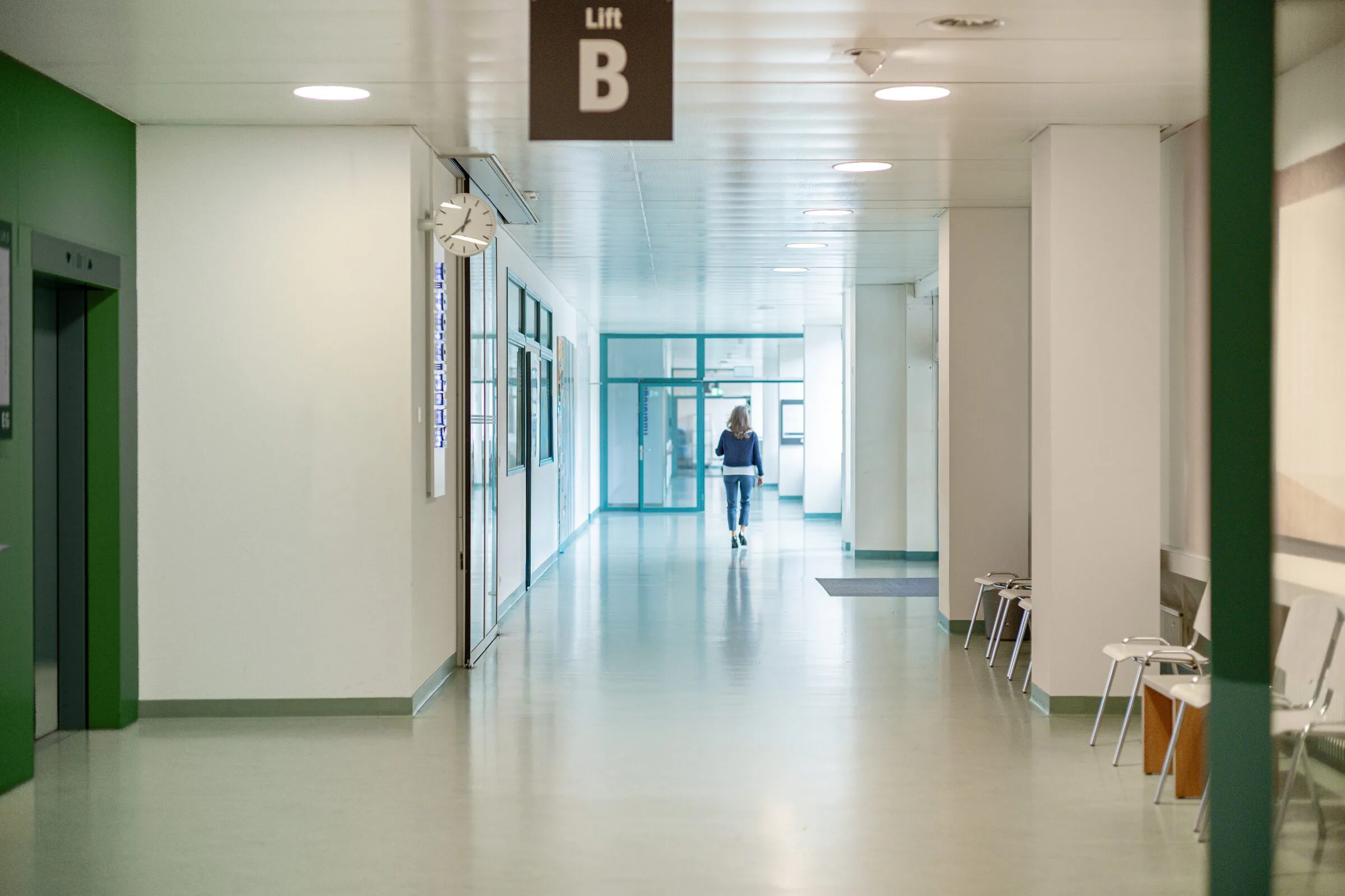 Heller Korridor eines Spitals, eine Person geht dem Tageslicht entgegen